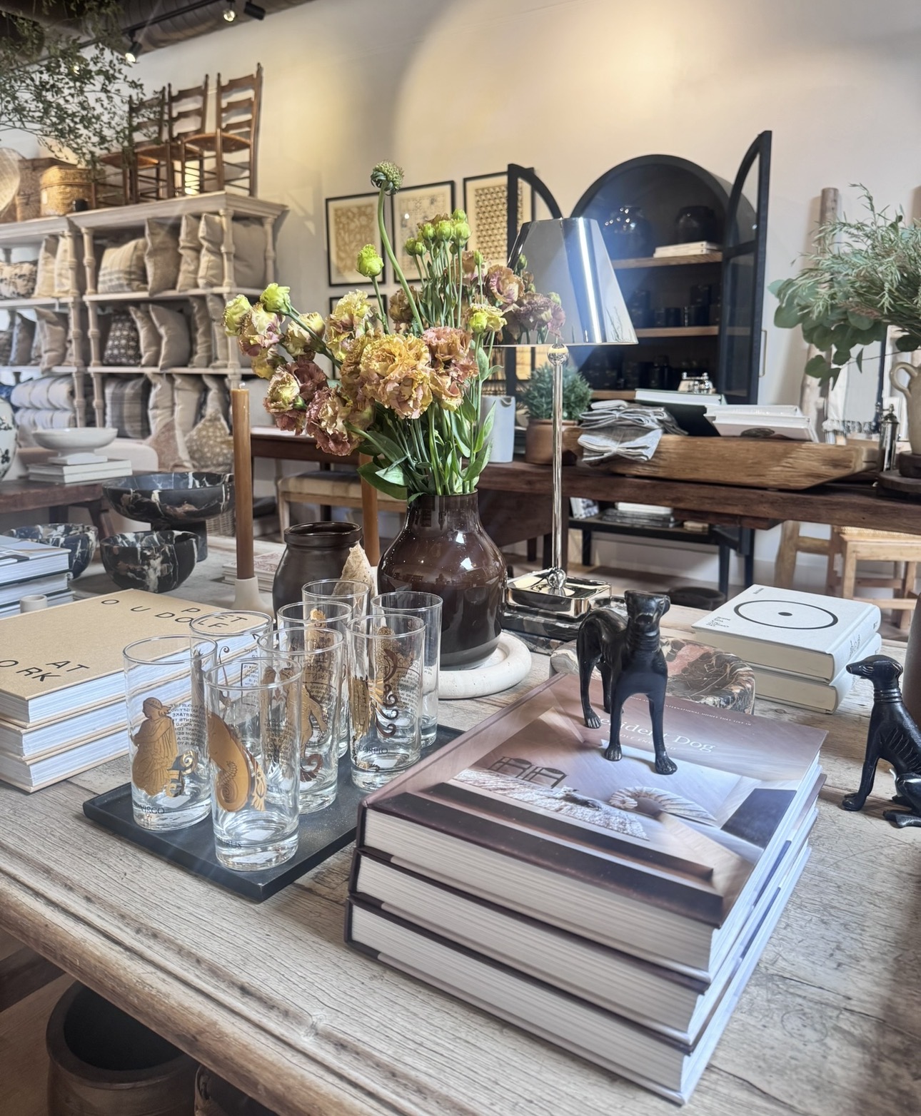 Styled tabletop with glassware, books, brass, and flowers