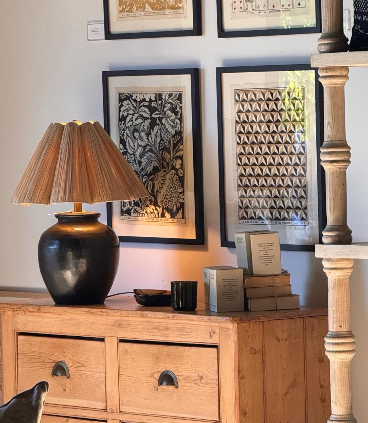 A dark ceramic lamp on a pine chest beneath framed prints